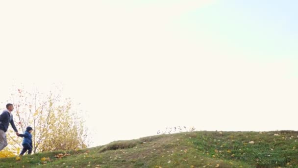 Lycklig familj med liten pojke går upp grön kulle i höstparken — Stockvideo