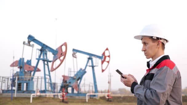 Trabalhador da indústria petrolífera com telefone no fundo da bomba de óleo — Vídeo de Stock