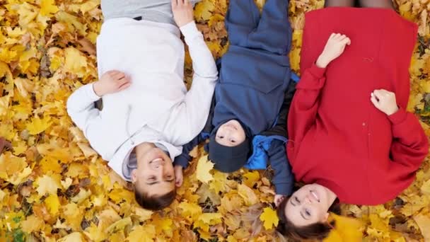 Веселая семья лежит на земле, а желтые листья опадают. — стоковое видео