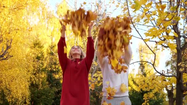 L'homme et la femme positifs jettent des feuilles jaunes sèches dans le parc — Video