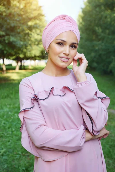 Hermosa mujer musulmana en un vestido rosa y un turbante sobre un fondo de árboles verdes — Foto de Stock