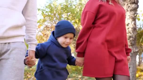 Милий маленький хлопчик стрибає гуляючи з батьками вздовж осіннього парку — стокове відео