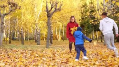 Anne, baba ve oğul yaprak döküyor. Parkta vakit geçiriyorlar.