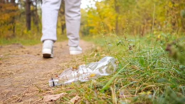 Unrecognizable woman throws a plastic bottle into the grass in the forest — Stock Photo, Image