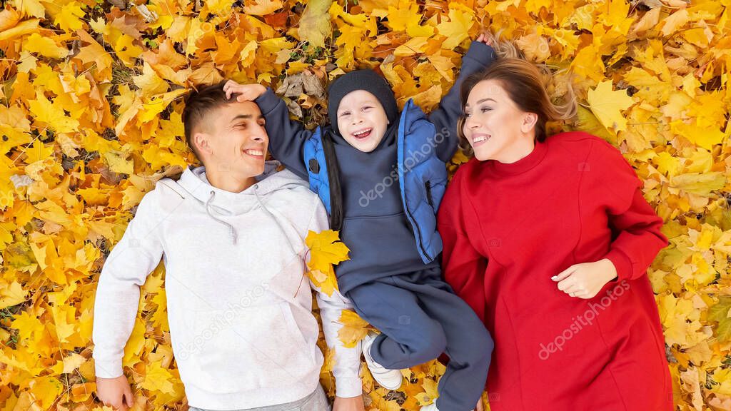 Mother father and boy spend time lying on yellow leaves