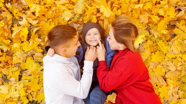 Matka a otec políbit a obejmout chlapce ležící na žlutých listech — Stock fotografie