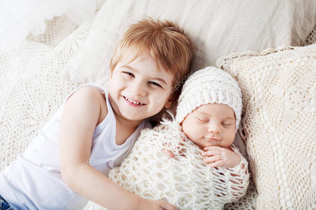 Portrait of newborn baby and elder brother. Young boy lying with newborn brother.