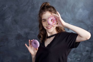 Siyah arka plan üzerine çörek gözleriyle kapsayan neşeli kız portresi. Çekici kız taze çörek holding ve tatlı şeylerle eğleniyor. İyi bir ruh hali, diyet kavramı.