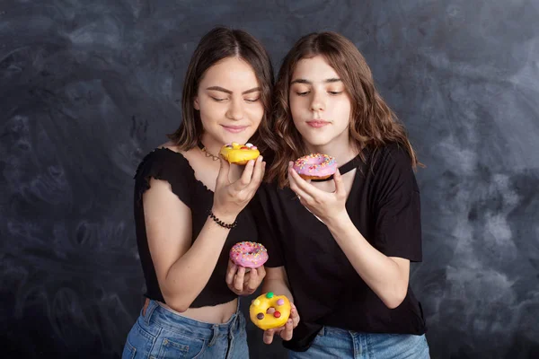 Mutlu oldukça genç kızlar eğleniyor çörek ile. Siyah arka plan üzerine çörek ile neşeli kız portresi. İyi bir ruh hali, diyet kavramı.