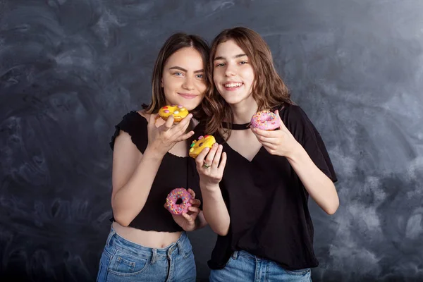 Mutlu oldukça genç kızlar eğleniyor çörek ile. Siyah arka plan üzerine çörek ile neşeli kız portresi. İyi bir ruh hali, diyet kavramı.