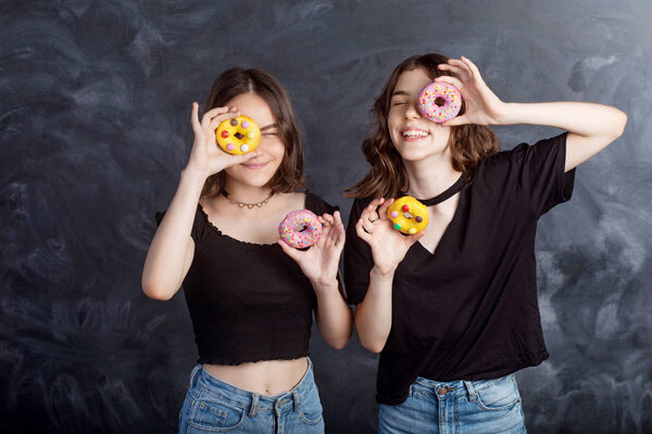 Happy pretty teenage girls with donuts having fun. Portrait of joyful girls with donuts on black background. Good mood, diet concept.