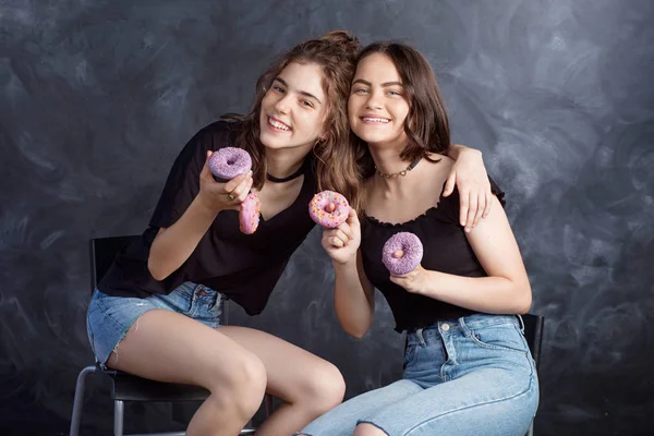 Mutlu oldukça genç kızlar eğleniyor çörek ile. Siyah arka plan üzerine çörek ile neşeli kız portresi. İyi bir ruh hali, diyet kavramı.