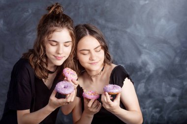 Mutlu oldukça genç kızlar eğleniyor çörek ile. Siyah arka plan üzerine çörek ile neşeli kız portresi. İyi bir ruh hali, diyet kavramı.