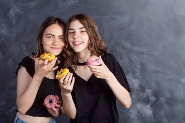 Mutlu oldukça genç kızlar eğleniyor çörek ile. Siyah arka plan üzerine çörek ile neşeli kız portresi. İyi bir ruh hali, diyet kavramı.