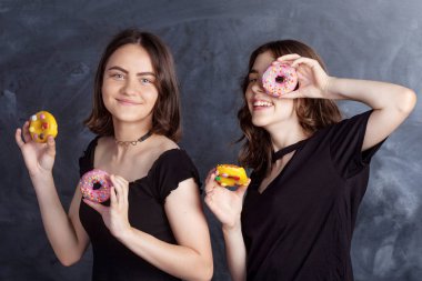 Mutlu oldukça genç kızlar eğleniyor çörek ile. Siyah arka plan üzerine çörek ile neşeli kız portresi. İyi bir ruh hali, diyet kavramı.