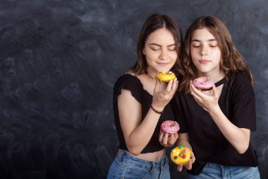 Mutlu oldukça genç kızlar eğleniyor çörek ile. Siyah arka plan üzerine çörek ile neşeli kız portresi. İyi bir ruh hali, diyet kavramı.
