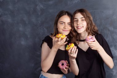 Mutlu oldukça genç kızlar eğleniyor çörek ile. Siyah arka plan üzerine çörek ile neşeli kız portresi. İyi bir ruh hali, diyet kavramı.