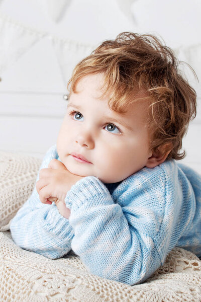 Portrait of happy adorable baby boy on the bed in his room. Thoughtful look up.