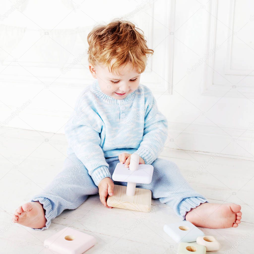 Child boy playing in his room with a wooden toy pyramid. Smiling cute boy with  natural toys. 
