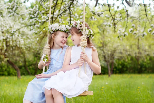 Дві милі дівчата розважаються на гойдалці в квітучому старому яблуневому дереві — стокове фото