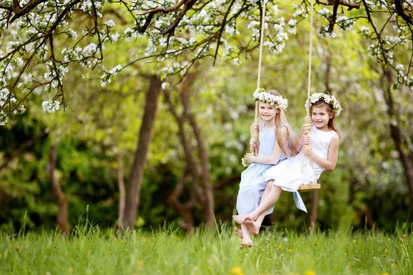 Zwei süße Mädchen haben Spaß auf einer Schaukel in blühenden alten Apfelbäumen — Stockfoto