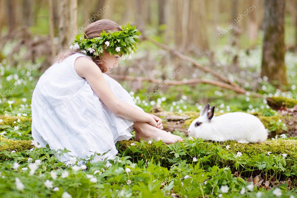 Beautiful  little girl in a white dress plaing with white rabbit in the spring wood. Easter time
