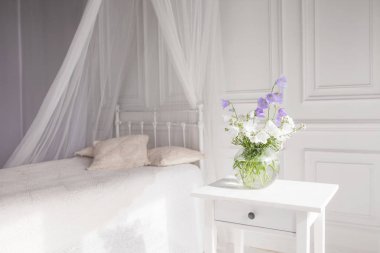 Lila ve beyaz floweers hafif rahat yatak odası iç ile aranjman. Beyaz duvar, beyaz keten, ışık battaniye ya da ekose ve yastık yatak.