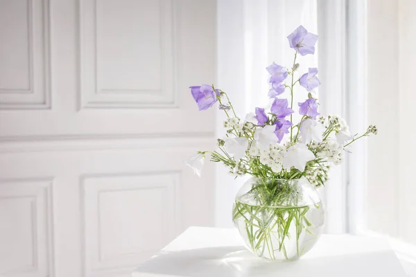 Glazen vaas met lila en wit floweers in lichte gezellige slaapkamer — Stockfoto