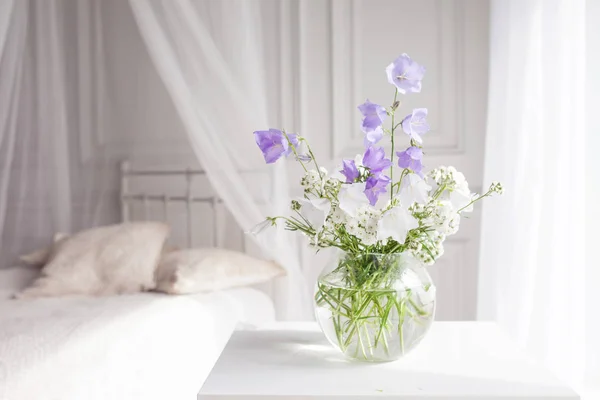 Glasvas med lila och vita floweers i ljus mysigt sovrum — Stockfoto