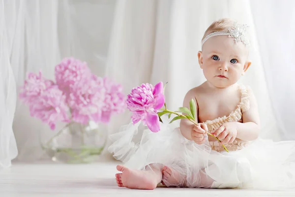Pequena menina bonita com olhos azuis senta-se em um chão com flores o — Fotografia de Stock