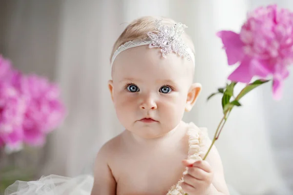 Pequena menina bonita com olhos azuis senta-se em um chão com flores o — Fotografia de Stock