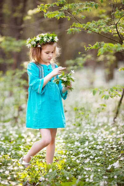 Vacker liten flicka i en blå klänning som promenader i våren trä — Stockfoto