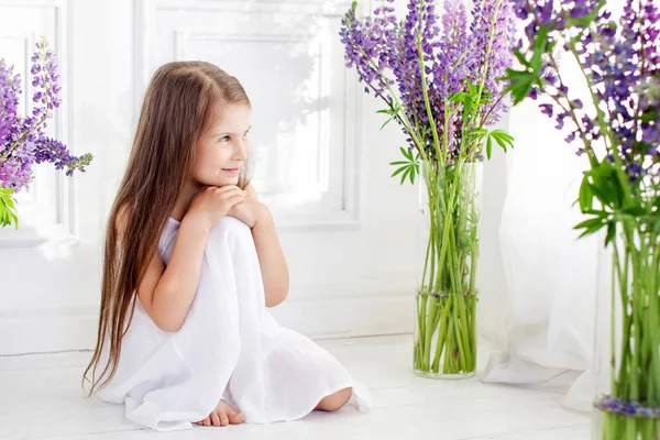 Beautiful little emotional girl siting  among violet flowers. A — Stock Photo, Image