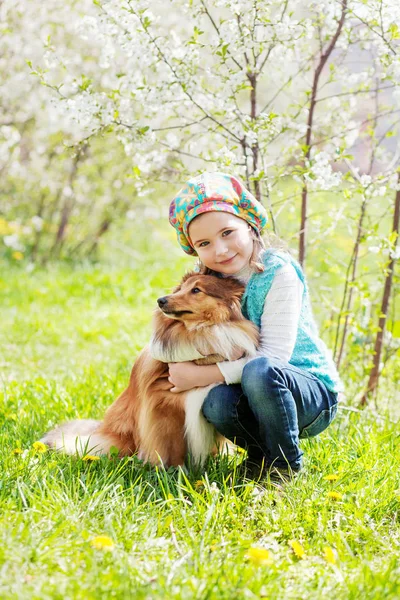 Милая улыбающаяся маленькая девочка обнимает собаку весной цветущей га — стоковое фото
