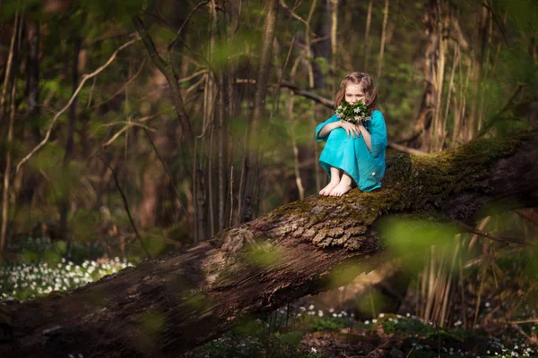 Красива маленька дівчинка в блакитній сукні, що ходить у весняному лісі — стокове фото