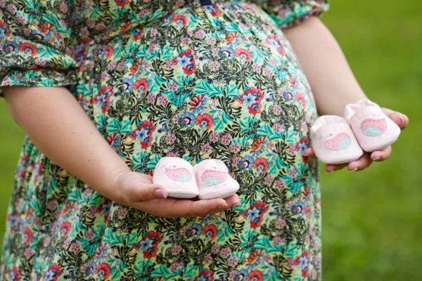 Großaufnahme einer schwangeren Frau mit Babyschuhen auf dem Bauch. Zwillinge — Stockfoto