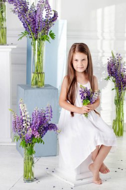 Beautiful little emotional girl sits among violet flowers. A flo clipart