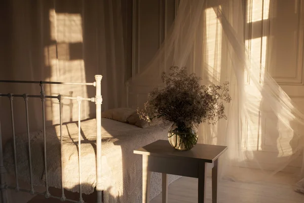 Sunset sunlight in the bedroom. A bouquet of flowers on a bedsid