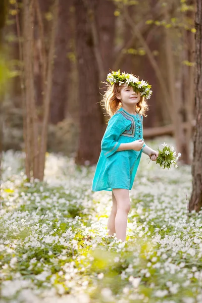 Vacker liten flicka i en blå klänning som promenader i våren trä — Stockfoto