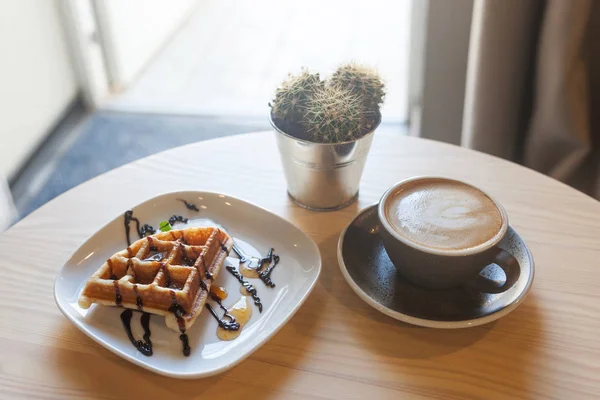 Tasse Kaffee und Teller belgische Waffeln auf hellem Holztisch — Stockfoto