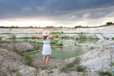 Açık deniz ve kumlu tepeleri olan bir gölün yanında şapkalı genç bir kadın. Gök gürültülü bulutlarla dolu doğal bir tabiat. Özgürlük ve neşe.