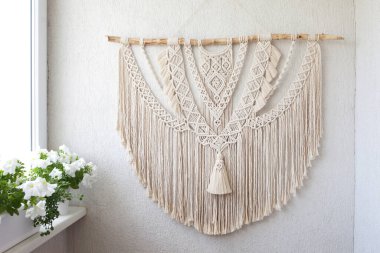 El yapımı makrome. Beyaz bir duvara asılı ahşap sopayla% 100 pamuk duvar süslemesi. Makrame örgü ve pamuk iplikleri. Kadın hobisi. ECO dostu modern örgü DIY doğal dekorasyon konsepti iç mekanda
