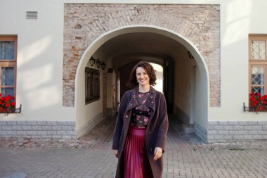 Güzel bir kadın, güneşli bir sonbahar ya da bahar gününde sokakta yürüyor. Kahverengi ceketli bir model..