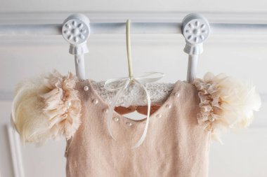 Beyaz arka planda yün ve açılış işlerinden bej elbiseler. Küçük kız için el yapımı bir askı.