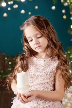 Işıkların arka planında uzun saçlı küçük bir kızın portresi. Elinde yanan mum tutan küçük bir kız. Noel, yeni yıl ve doğum günü kutlaması konsepti. Kış tatili Boşluğu kopyala