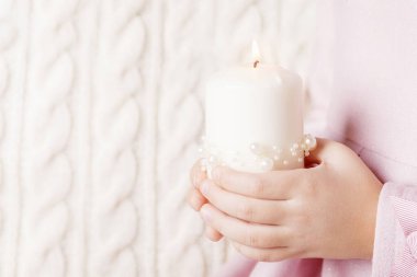 Bir kızın ellerinde yanan bir mum. Noel mumu. Noel dekoru. Çocuğun elleri güzel bir mumu ateşle tutuyor. Hafif arkaplan. Boşluğu kopyala
