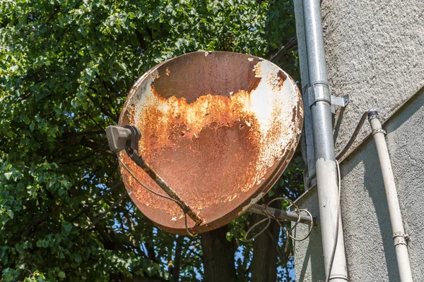 An old rusty TV dish on a background of green leaves on a bright Sunny day