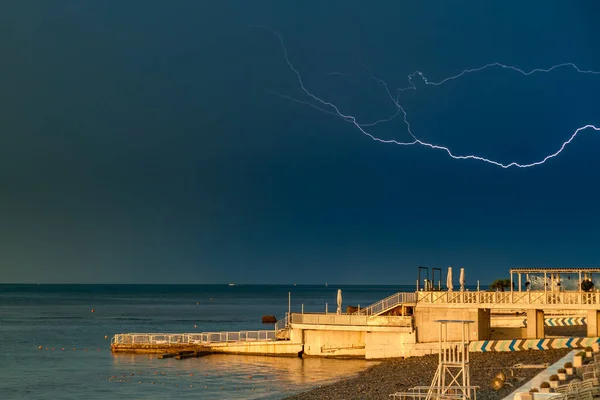 Lightning over the beach, pier and sea. Solar sunset light