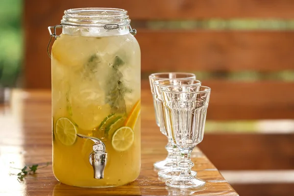 Glass can with fruit drink and empty faceted glasses