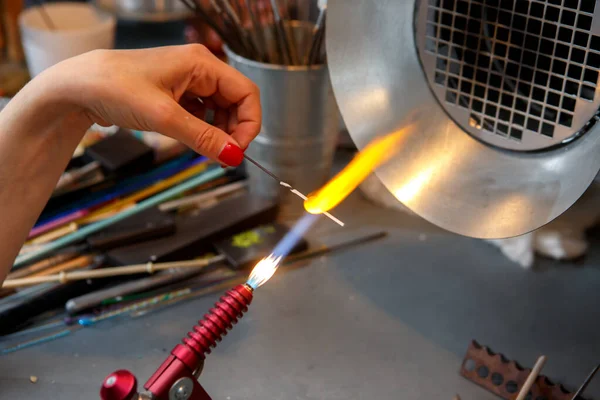 The artist heats the glass with a gas burner. The process of making glass jewelry. Master's hands close up